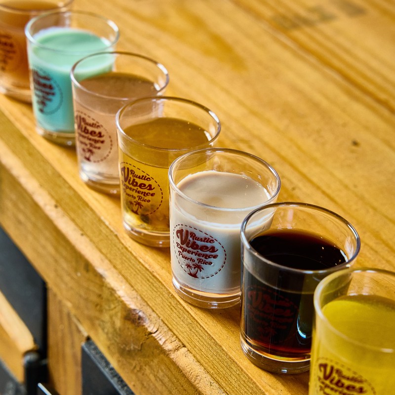 Row of seven colorful shots on a wooden surface.